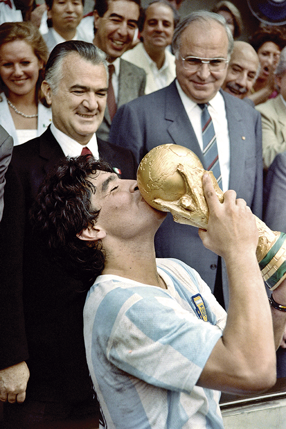 Argentina's soccer star team captain Diego Maradona kisses the World Soccer Cup won by his team after a 3-2 victory over West Germany on June 29, 1986 at the Azteca stadium in Mexico City watched by Mexican President Miguel de La Madrid (L) and West German Chancellor Helmut Kohl. (Photo by Dominique FAGET / AFP) (Photo by DOMINIQUE FAGET/AFP via Getty Images)